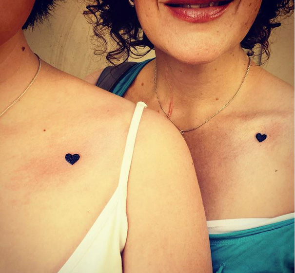 Mother-daughter tattoos showing small black hearts on their shoulders, symbolizing an unbreakable bond.