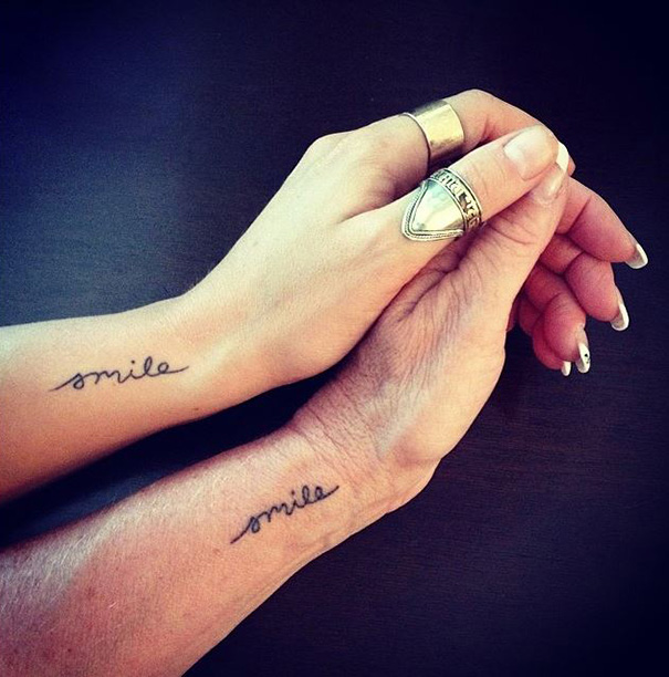 Mother-daughter tattoos on wrists, both reading "smile," showcasing their unbreakable bond.