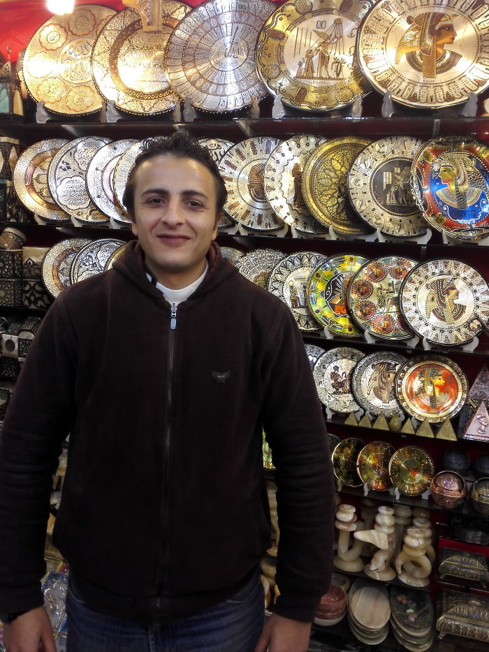 Man standing in front of a display of decorative plates and souvenirs, illustrating celebrity doppelganger animals concept.