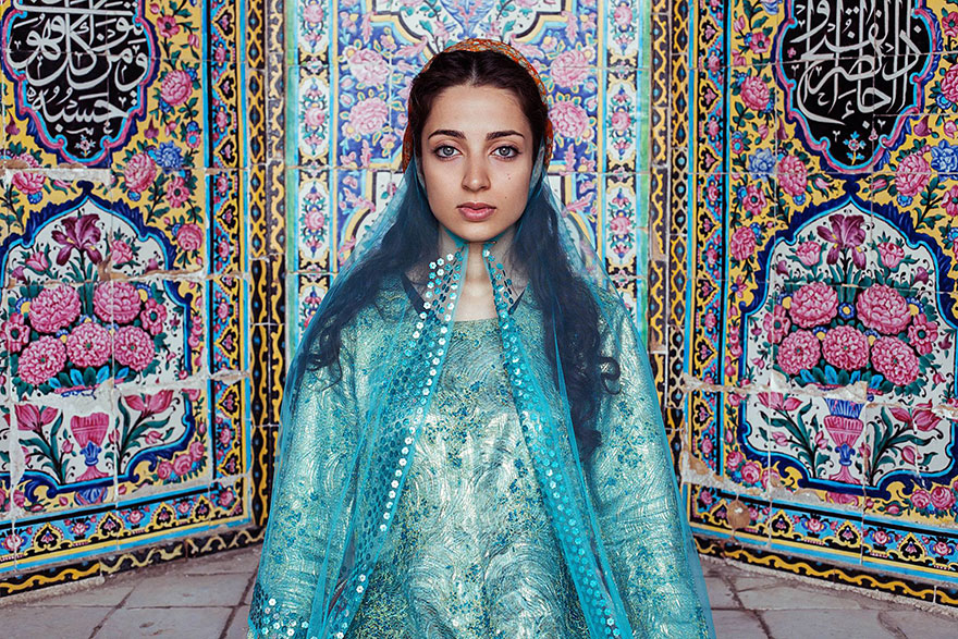 Woman in blue traditional attire poses against a vibrant tile backdrop, captured by Romanian photographer showcasing global beauty.