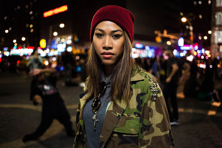 Woman in camo jacket and red beanie in city at night, showcasing Romanian photographer's global beauty project.