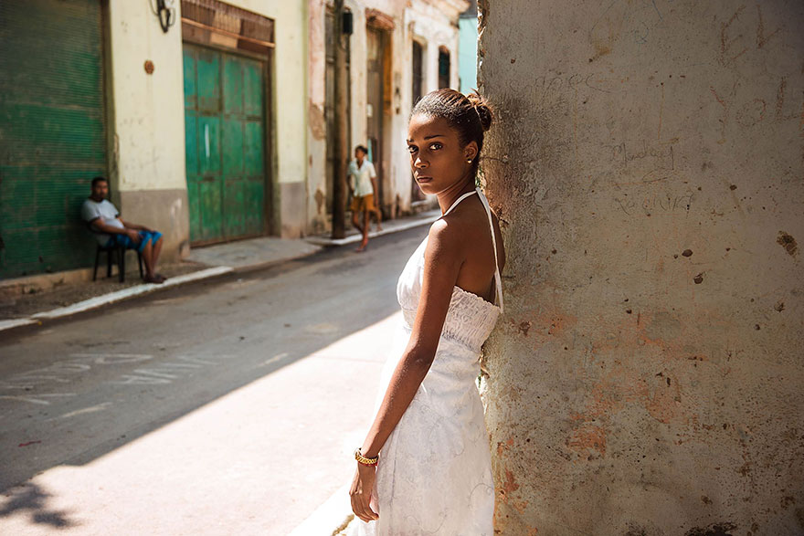 Woman in white dress stands against a wall, showcasing global beauty through Romanian photographer's lens.