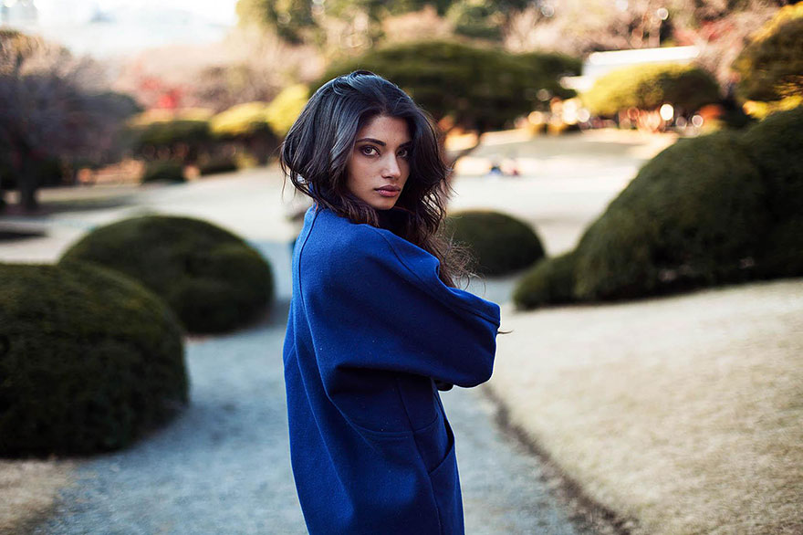 Woman in a blue coat posing outdoors, showcasing global beauty through Romanian photographer's lens.