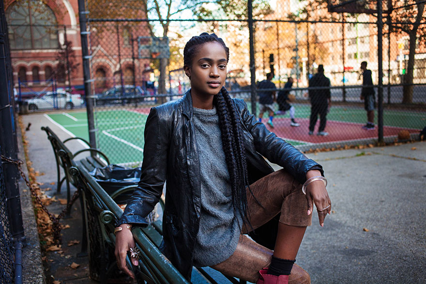 Woman in urban setting, showcasing global beauty as captured by Romanian photographer, seated near a basketball court.