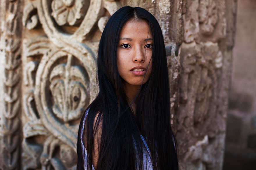 Woman from Romania project showing global beauty, standing by intricate stone carving.