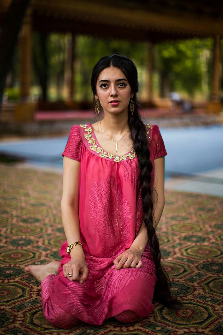 Woman from Romania in a vibrant pink dress showing beauty worldwide, sitting on an ornate carpet.