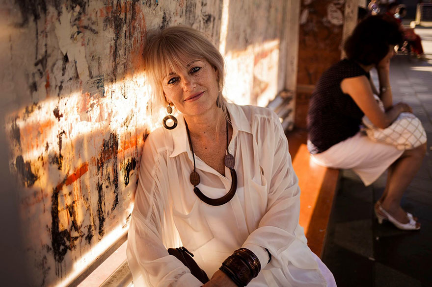 Woman in a white blouse, sitting against a graffiti wall, photographed by a Romanian photographer showcasing universal beauty.