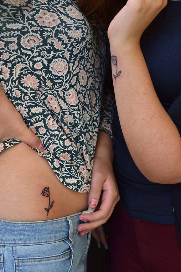Two sisters showcasing matching flower tattoos, symbolizing their bond.
