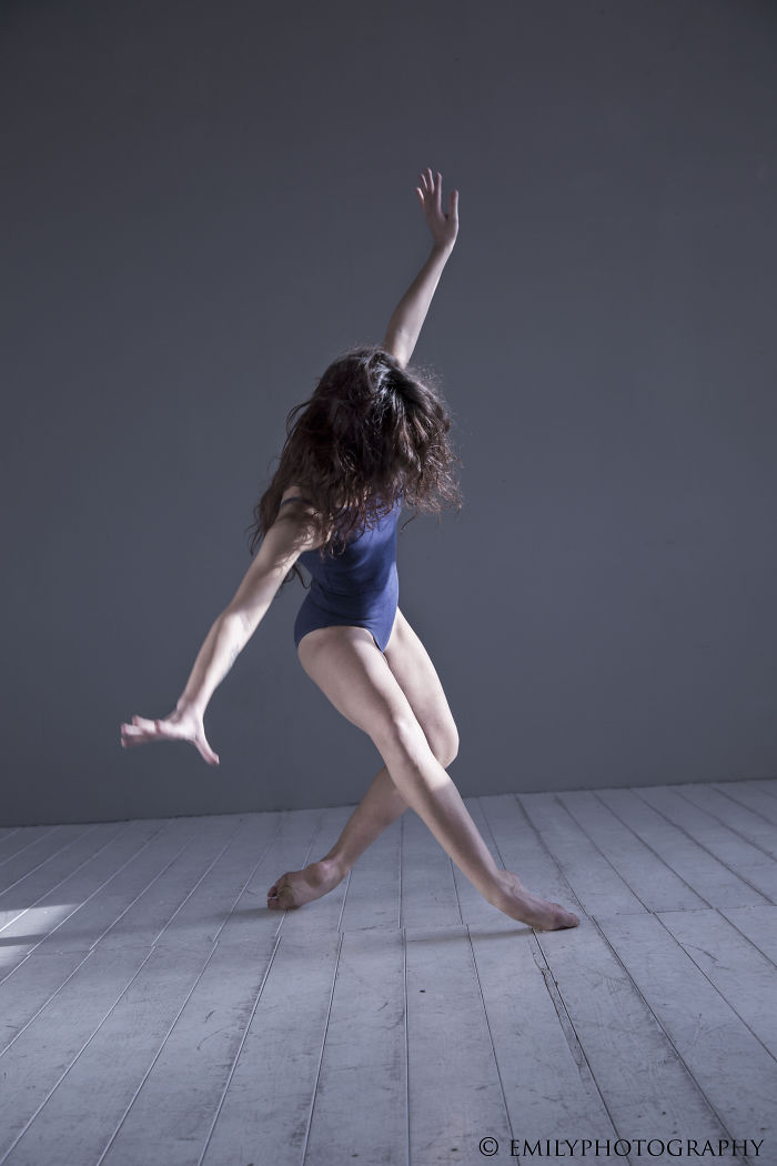 Ballet dancer in a navy leotard striking a graceful pose on a wooden floor.