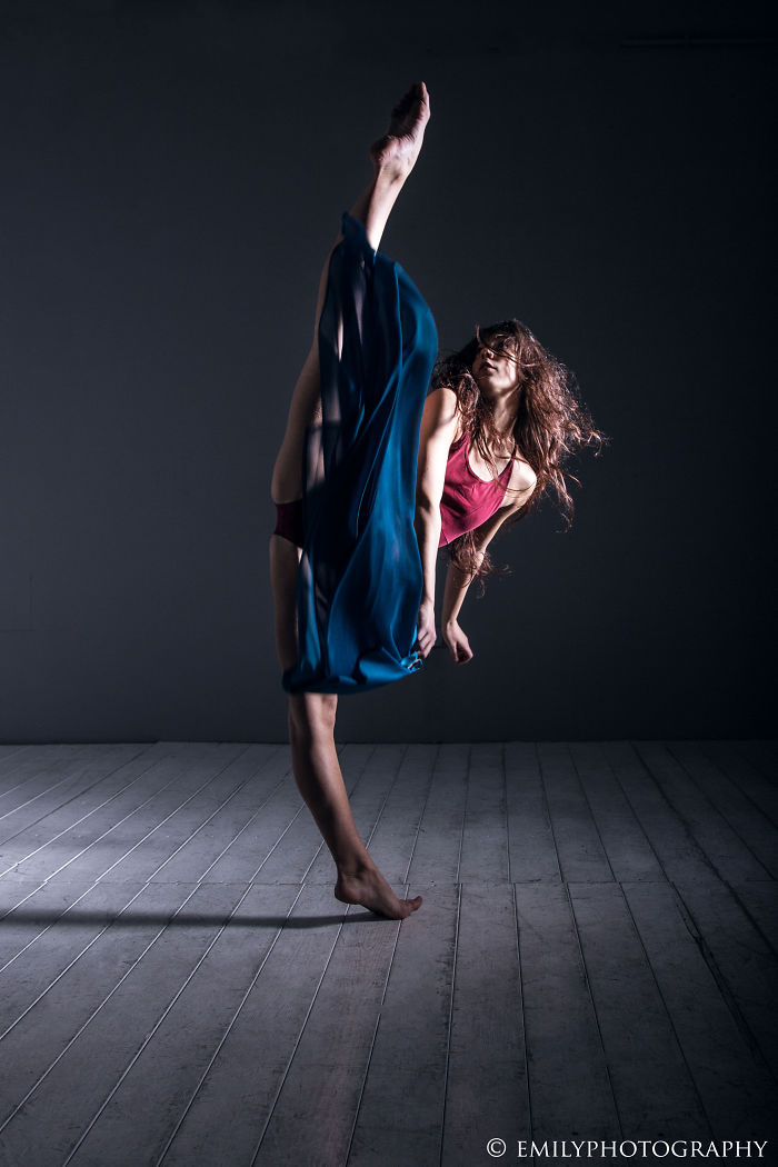 Ballet dancer performing a high kick gracefully in a dimly lit studio.