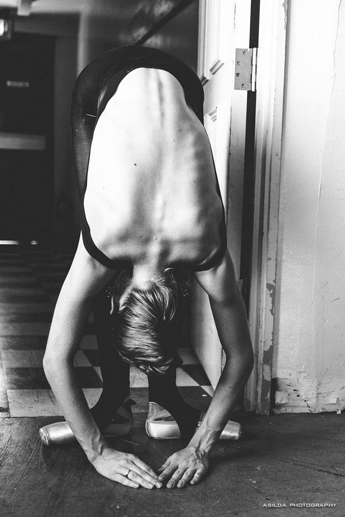 Ballet dancer bends forward in a hallway, showcasing dedication and strength.