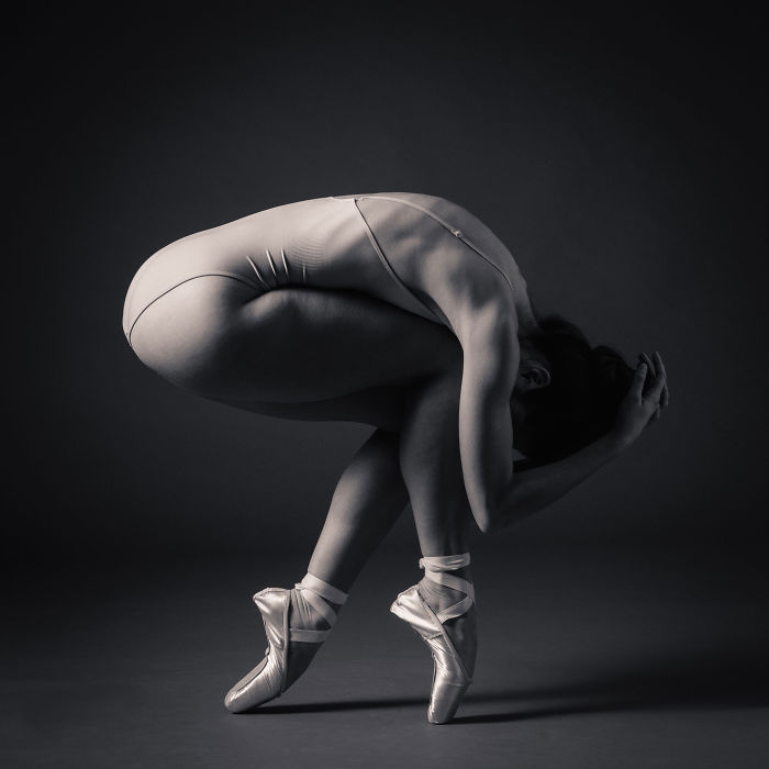 Ballet dancer in an elegant pose on pointe shoes, showcasing flexibility and strength in a minimalist setting.