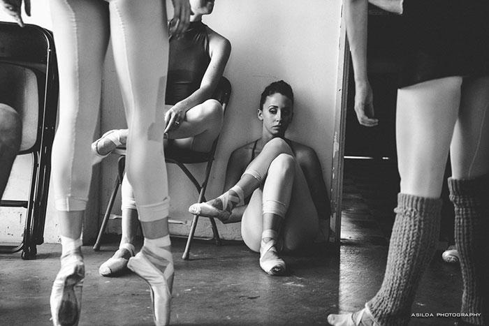 Ballet dancers resting backstage, depicting the physical demands and dedication behind the cost of applause.