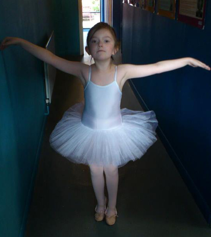 Young ballet dancer in a white tutu practicing ballet pose in a hallway.