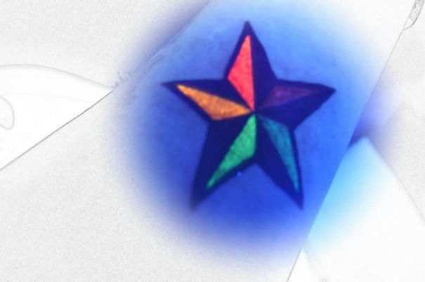 Glow in the dark tattoo of a colorful star, visible under black light.