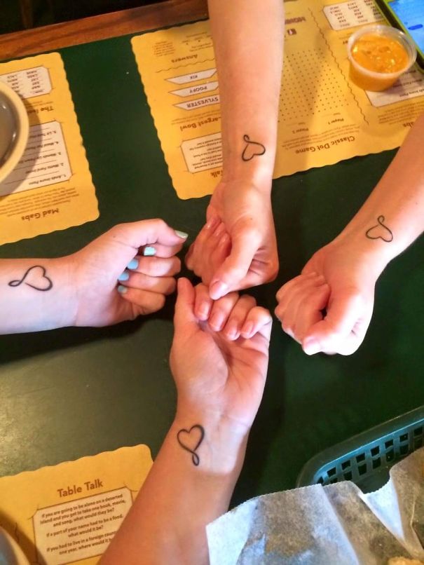 Four arms with matching heart tattoos symbolizing sister bond.