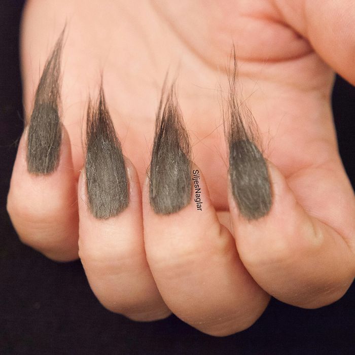 Close-up of hand with furry nails featuring long, hairy black fibers as part of the furry nails beauty trend.