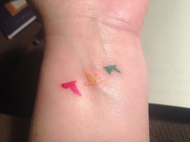 Minimalist tattoo of three colorful birds on a wrist.