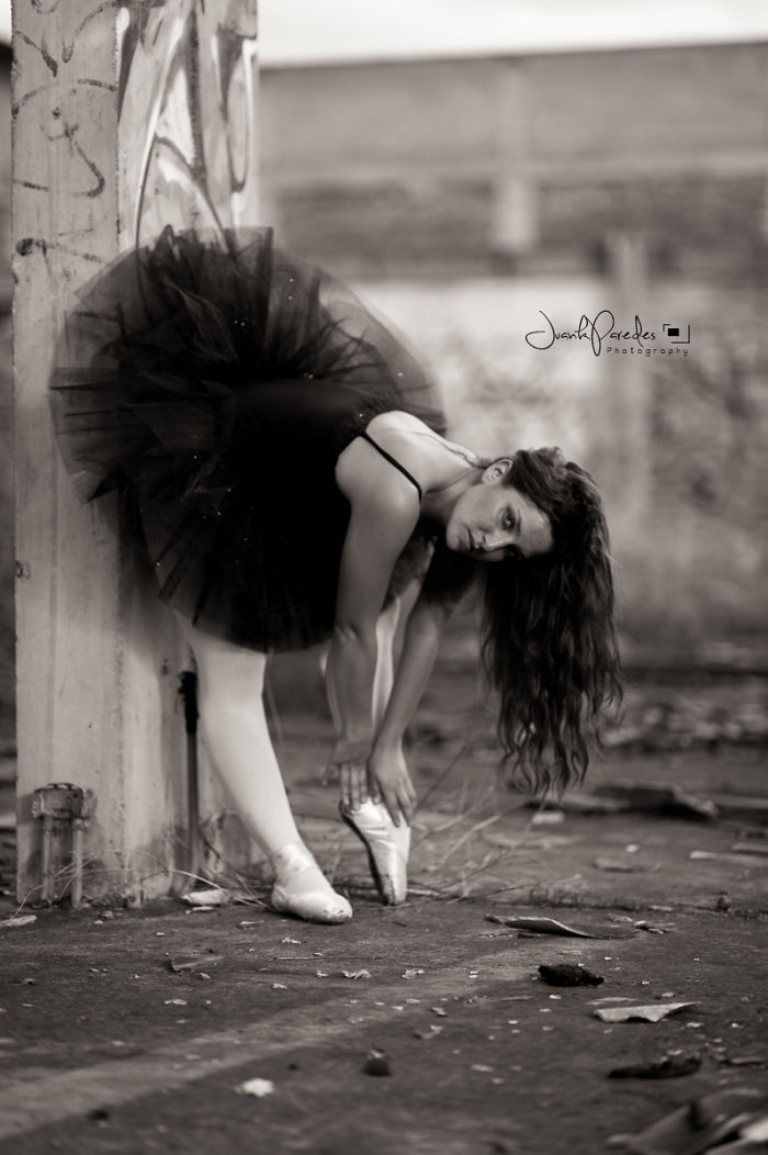 Ballerina in a black tutu adjusting pointe shoes, representing the cost of applause in ballet performance.