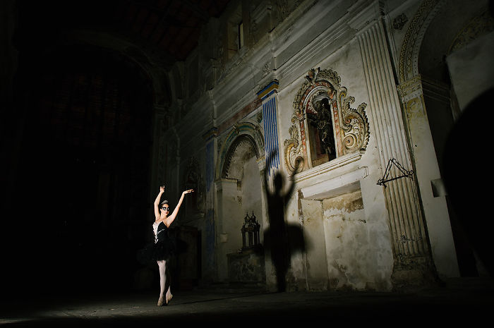 Ballet dancer performing in an ornate, dimly lit theater, casting a dramatic shadow on the wall.