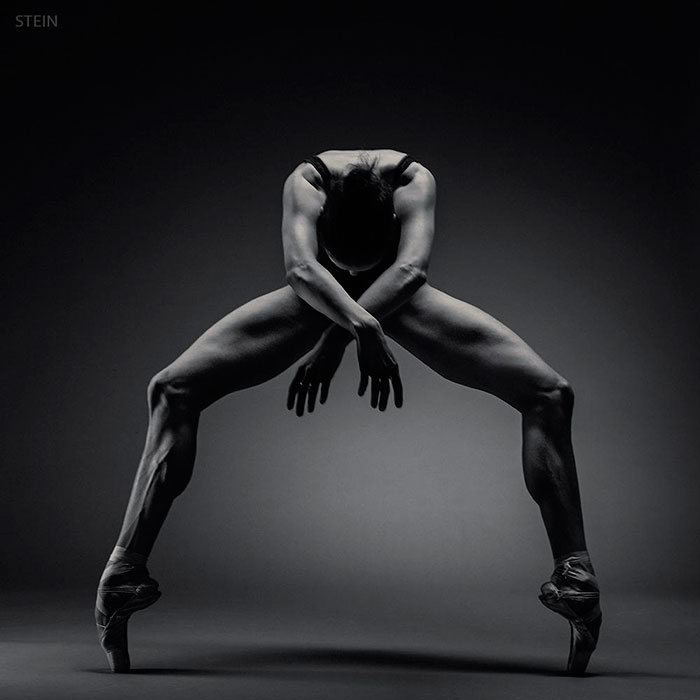 Ballet dancer in dramatic pose, demonstrating strength and grace on pointe against a dark background.