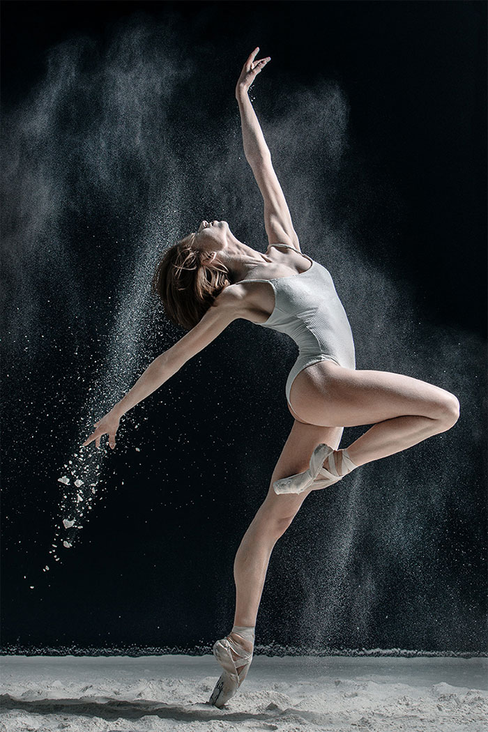 Ballet dancer performing a dramatic leap with dust surrounding her in an artistic display.