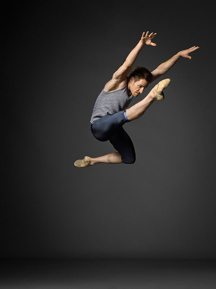 Ballet dancer performing a high jump against a dark background, showcasing the art of ballet.