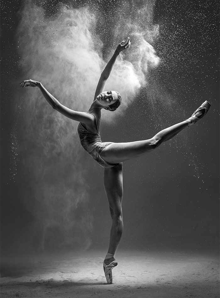 Ballet dancer in a graceful pose with floating powder in a dramatic black-and-white photo.