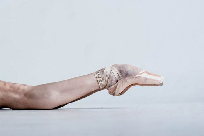Ballerina's foot in pointe shoe, showcasing the cost of applause in ballet, resting on a smooth white surface.