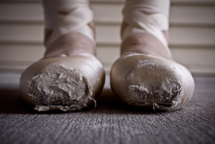 Worn ballet pointe shoes on a dancer's feet, highlighting the cost and dedication of ballet.
