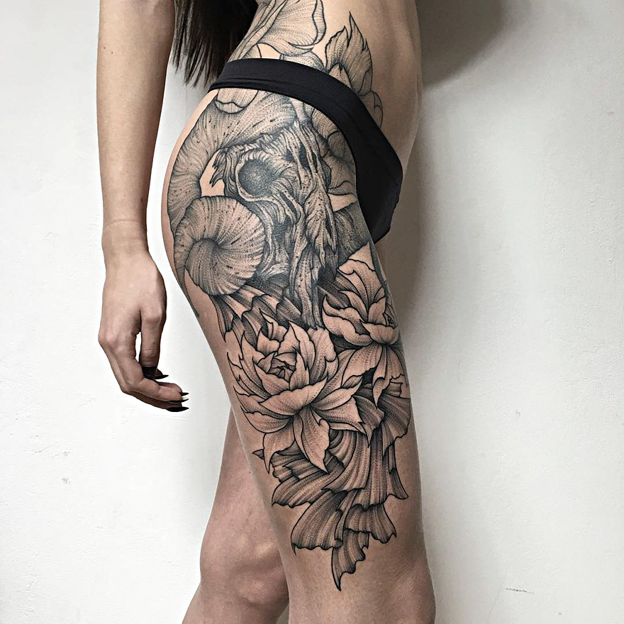 Eerie creature tattoo by Russian artist on woman's leg, featuring skull and floral design.