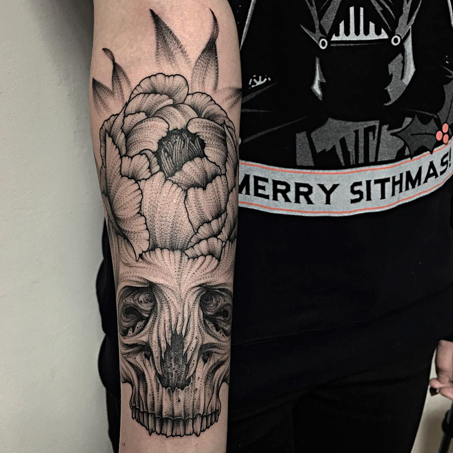 Dark eerie creature tattoo on arm by Russian artist, featuring a skull with floral elements.