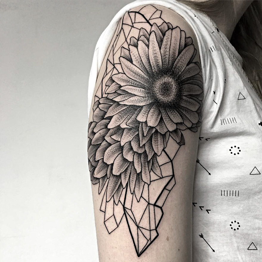 Tattoo of a sunflower and geometric shapes on an upper arm, created by a Russian artist.