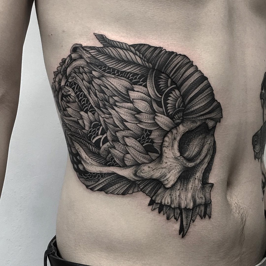Dark and eerie creature tattoo on a man's side, detailing an intricate skull and feather design.
