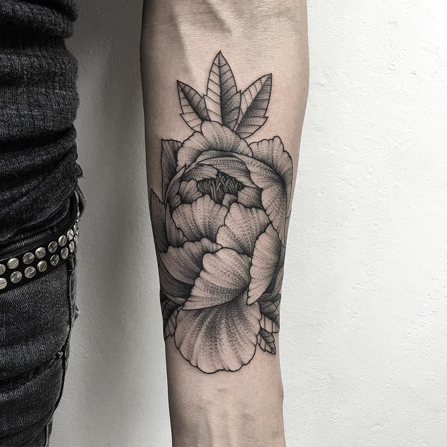 Russian artist's dark tattoo of floral design on forearm, showcasing intricate shading and detail.