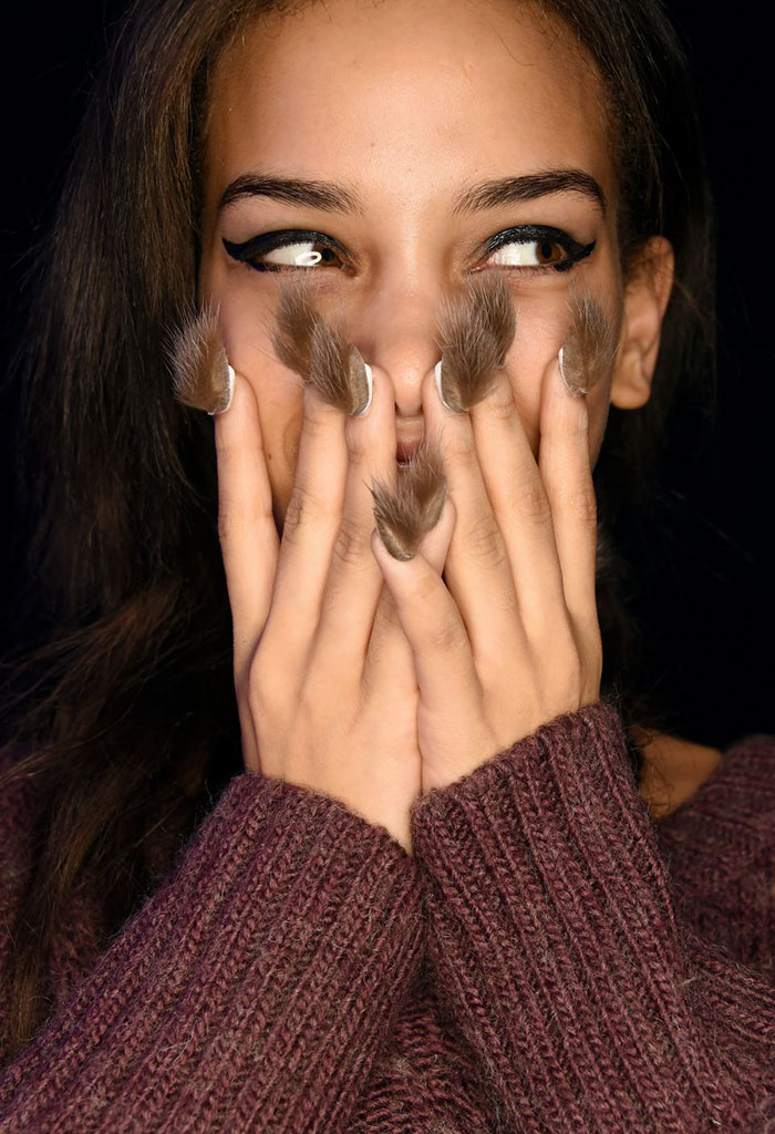 Close-up of a woman with furry nails covering her mouth, showcasing the unique hairy nail trend in fashion beauty.