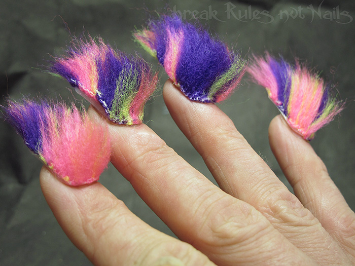 Furry nails with bright purple, pink, and green fuzzy textures create the hairiest nail trend on a person’s hand.
