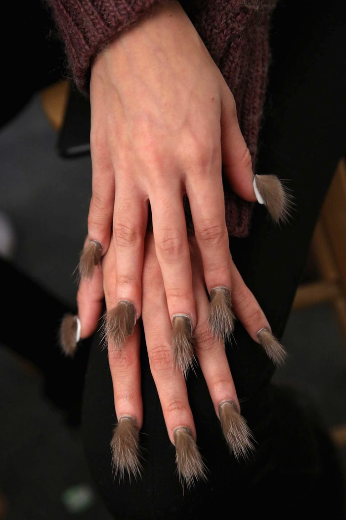 Hand with furry nails featuring long hair-like extensions as a bold fashion statement on each fingertip.