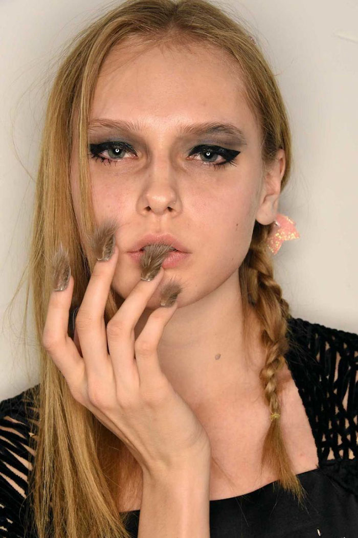 Model with furry nails trend, featuring long faux fur nail art and bold eye makeup in a close-up portrait.