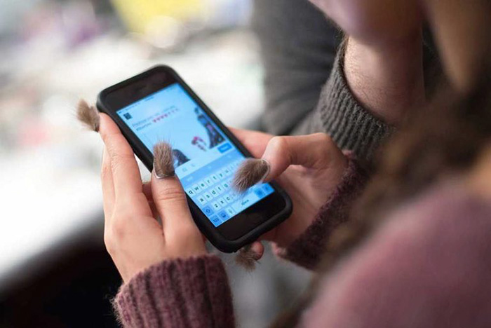 Close-up of hands with furry nails using a smartphone, showcasing the latest furry nails trend in fashion.