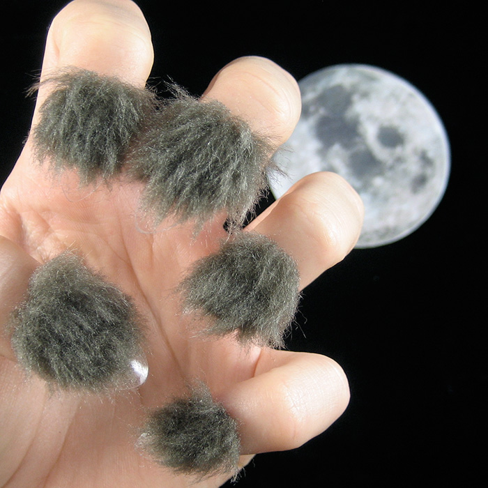 Hand with furry nails covered in gray hair-like texture against a dark sky background with a full moon visible.