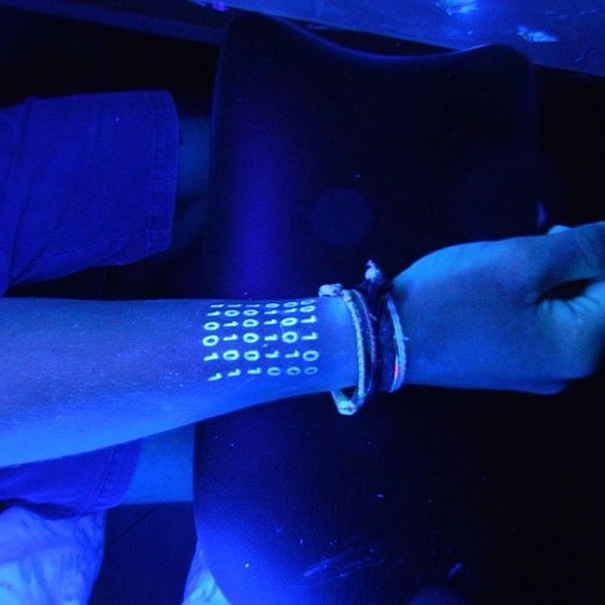 Glow in the dark tattoo of binary code visible under black light on a forearm.