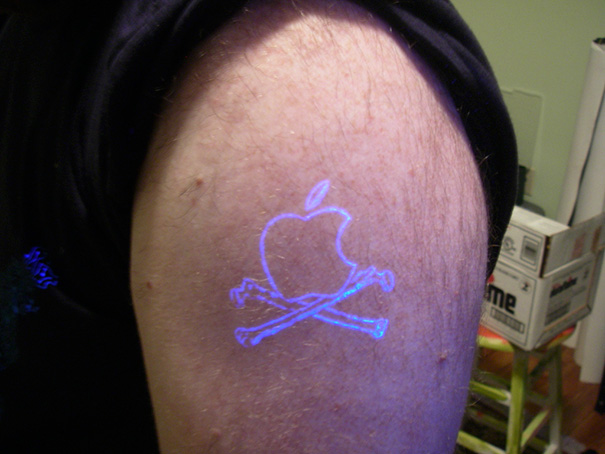 Glow in the dark tattoo of an apple with crossed bones, illuminated under black light.