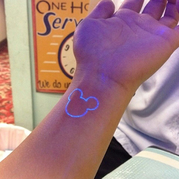 Glow in the dark tattoo on wrist, visible under black light, designed with a minimalist mouse silhouette.