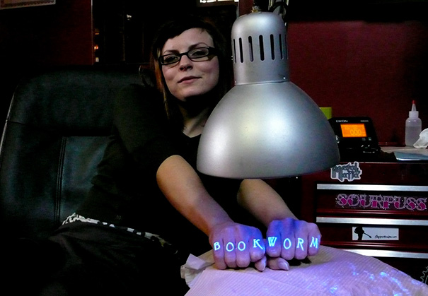 Person with glow in the dark tattoos reading "BOOKWORM" visible under black light.