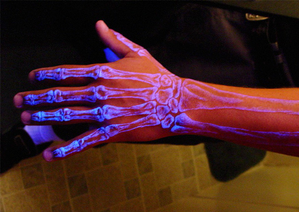 Glow in the dark tattoo of a skeletal hand visible under black light on a person's arm.