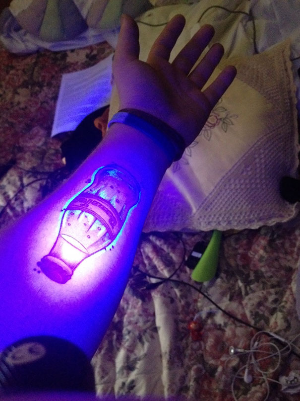 Glow in the dark tattoo of a bottle on forearm, illuminated under black light.