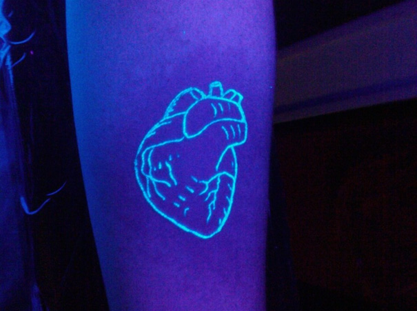 Glow in the dark tattoo of a heart design on an arm, visible under black light.