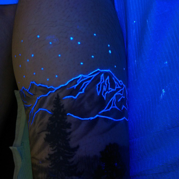 Glow in the dark tattoo with mountains and stars, illuminated under black light.