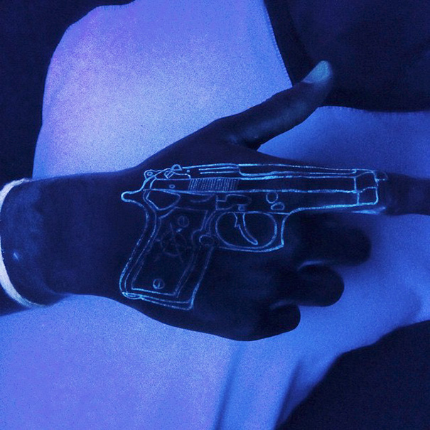 Hand with glow in the dark tattoo of a gun, visible under black light.